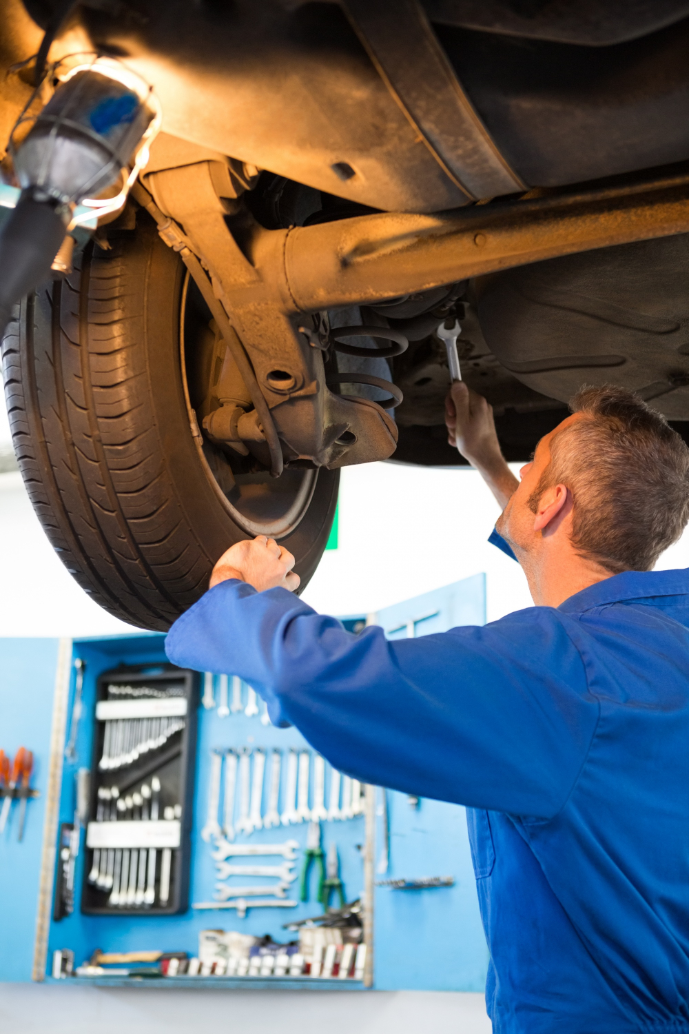 Mechanik pracujący pod podniesionym samochodem podczas kontroli i naprawy elementów przy kole