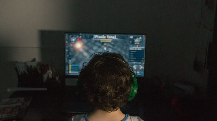 Dziecko siedzące tyłem przed komputerem w słuchawkach, grające w grę